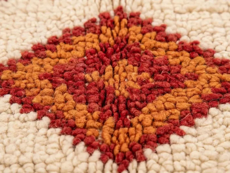 A close-up view showing the natural loop and wool pile detail of a cream Berber rug with warm terracotta orange diamond patterns.