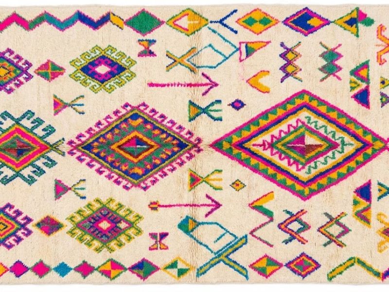 An overhead view of a handcrafted cream Azilal rug displaying vibrant, multicolored geometric patterns.