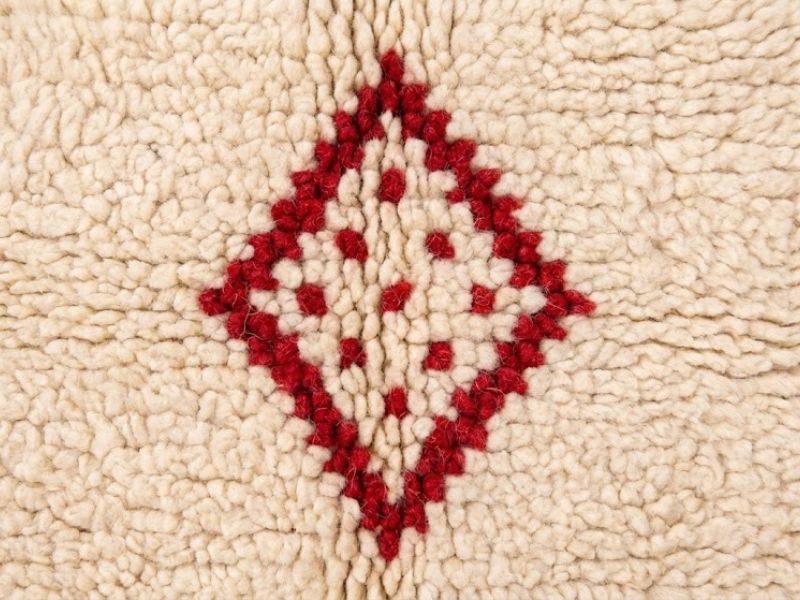 A plush cream Berber wool rug featuring a delicate hand-knotted red diamond pattern.